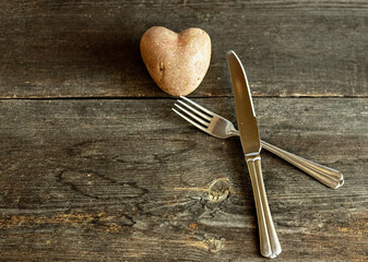 Red potatoes in the shape of a heart on a wooden background with a fork and knife. The concept of...