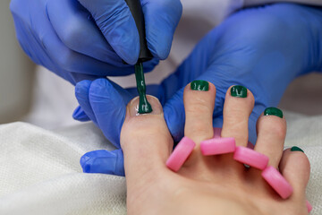 The nail artist covers the toenails with decorative nail polish. Aesthetic pedicure in the salon.