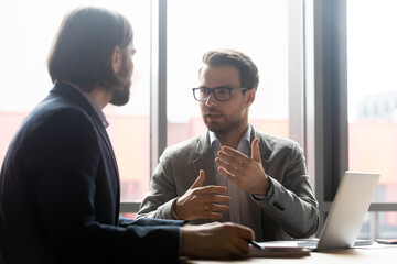 Skilled 30s businessman in eyeglasses discussing project with focused male partners at...