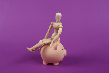 Wooden puppet sitting on piggy bank on a purple background. Save money concept