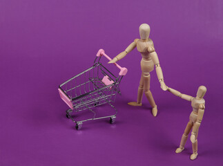 Two wooden puppets with supermarket trolley shopping together on purple background
