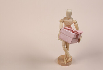 Wooden puppet mannequin holding a gift box on beige background.