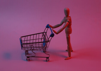Two wooden puppets with supermarket trolley in red neon light