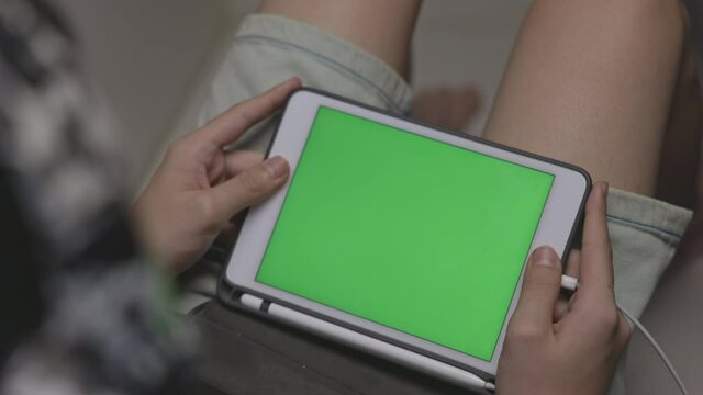 Anonymous hands holding using tablet pad touch screen technology with green screen frame, browsing online reading on portable device sitting in living room interior,  shoulder view, Dolly shoot.