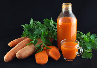 Carrot juice in a bottle and in a mug, carrots and parsley on a black background.