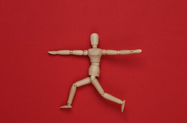Wooden puppet in asana warrior 2 pose on red background. Harmony, yoga, healthy lifestyle