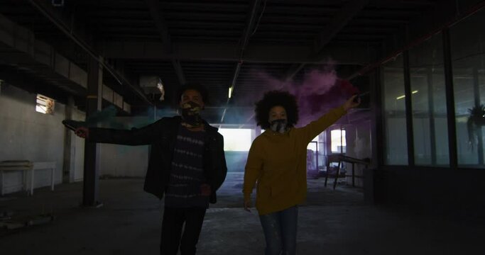Mixed race man and woman holding blue and purple flares running through an empty building