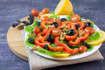 On a white plate, vitamin fresh vegetable salad with lettuce, red peppers, olives, walnuts, cherry tomatoes and dried raisins. For a hearty and healthy snack.