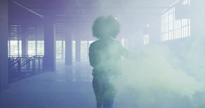 Mixed race woman holding green flare walking through empty building