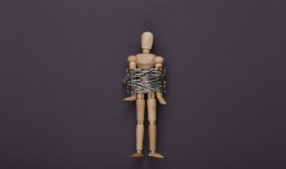 Wooden puppet wrapped in a steel chain on gray background. Top view