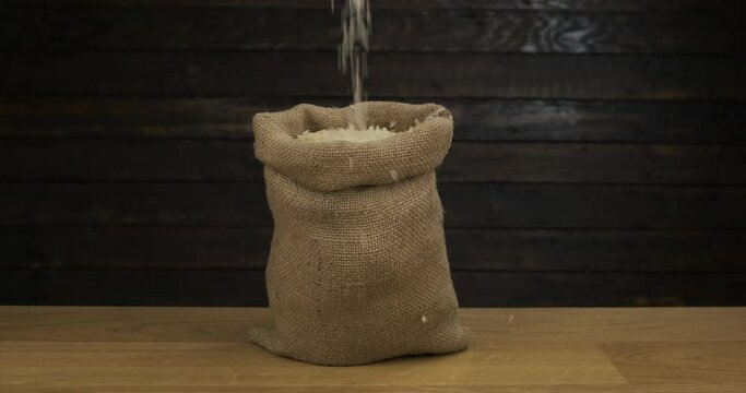 Open classic burlap sack, filled with falling rice grains. Seed in sack on wooden table.