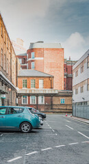 Fototapeta na wymiar paisaje británico urbano con perspectiva de varios edificios de ladrillo rojo y cristaleras y un coche azul estacionado