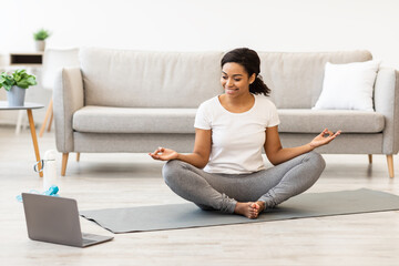 Black woman practising yoga having online tutorial on laptop