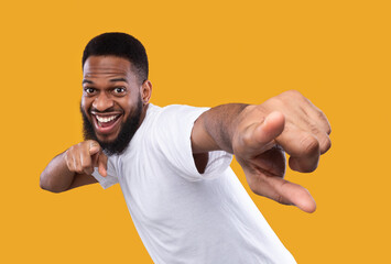 Funny african man posing pointing fingers at camera, yellow background