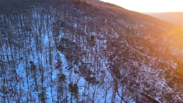 Rising above a forested mountain covered in snow at sunset.