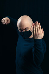 Portrait of a bald man in a black medical mask on a dark background. A man in a belligerent stance...