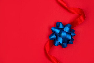 Top view on decorative blue ribbon bow on red background with copy space for text. Giving presents concept. Festive composition for greeting card or holidays sale background. Selective focus