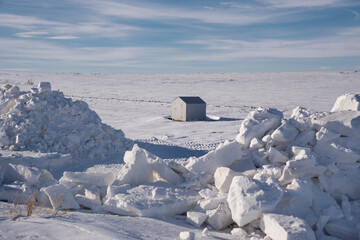View of a winter snow field with a lone structure and large piles of snow. The concept of winter