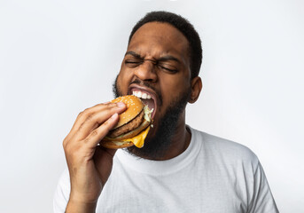 African Man Biting Burger Enjoying Junk Food Over White Background