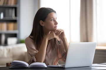 Close up thoughtful dreamy young woman looking to aside, sitting at desk with laptop, pensive...
