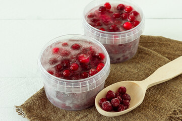 Frozen healthy cranberries in a plastic containers with cube of ice on wooden background