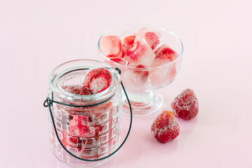 Ice cubes with strawberries on pink background.