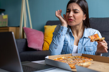 A smiling young woman is eating pizza and having a toothache in the living room.