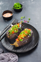Baked stuffed eggplant with different vegetables, tomato, pepper, onion and parsley in round black plate on dark stone or concrete table background. Top view.