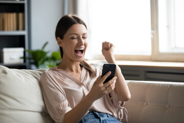 Close up overjoyed woman holding phone, screaming with joy, showing yes gesture, excited young...