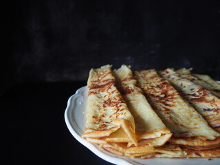 Homemade crepes, french crêpes, traditionally made for Candlemas, on black background, horizontal picture and space for text on the left