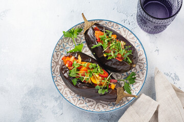 Baked stuffed eggplant with different vegetables, tomato, pepper, onion, microgreens and parsley on gray stone or concrete table background. Top view.