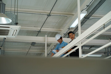 Asian engineer wearing hard hat talking with business man in formal suit in the factory