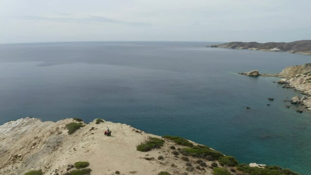 Revealing drone shot of beautiful scenic coastal cliffs in Ios, Greece with Couple on quad bike