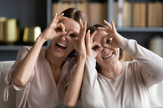 Head shot portrait close up grownup daughter and mature mother making binoculars gesture, happy young woman and elderly mum posing for funny family photo, looking at camera, having fun together