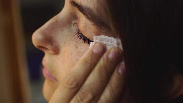 young Woman is removing makeup from her face cleaning facial skin, portrait closeup. Girl is wiping face skin. Skincare concept.
