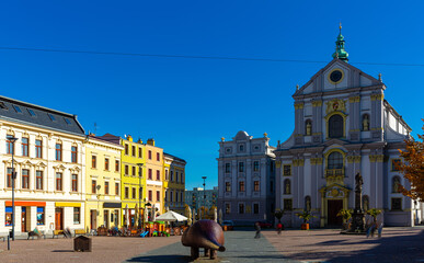 Obraz premium View of Lower Square in Opava historic centre with Church of St. Adalbert and piece of modern art called Spy on sunny autumn day, Czech Republic