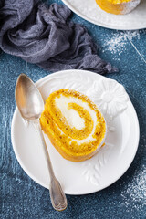 Dessert pumpkin roll with butter cream and orange for the festive table on dark blue concrete background. Selective focus.