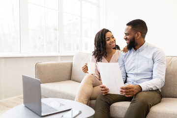 Fototapeta premium Positive black couple reading documentation at home, checking agreement