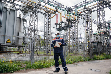 An electrical substation engineer inspects modern high-voltage equipment in a mask at the time of pondemia. Energy. Industry