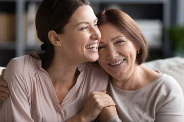 Close up head shot portrait smiling mature mother and grownup daughter cuddling, family enjoying...