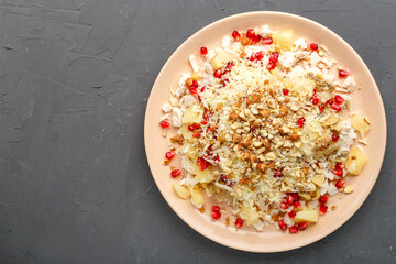 A plate with salad with chicken, pineapple, pomegranate and nuts on a concrete background.