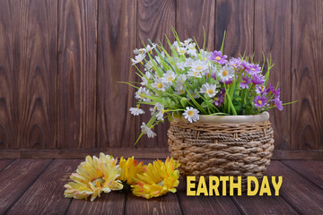 Plastic flowers on a wooden background and the inscription earth day