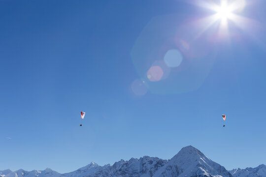 Dramatic lens flare highlights two paragliders above the snow capped mountains