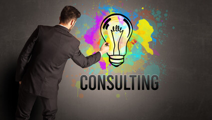 businessman drawing colorful light bulb with CONSULTING inscription on textured concrete wall, new business idea concept