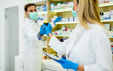 Fototapeta premium Male and female pharmacists with protective mask on their faces working at pharmacy. Medical healthcare concept.