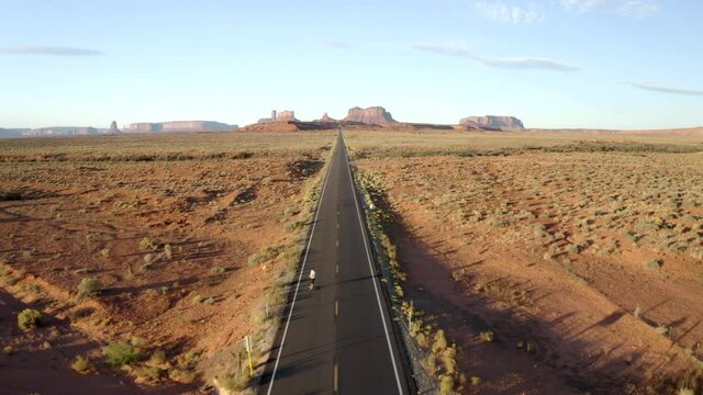 Smooth Drone footage of man skateboarding in Monument valley along forest Gump highway in Utah