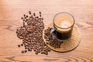 Cup of coffee. Black coffee brew in glass cup and coffee beans on wooden table background. Dark roast espresso coffee mug closeup