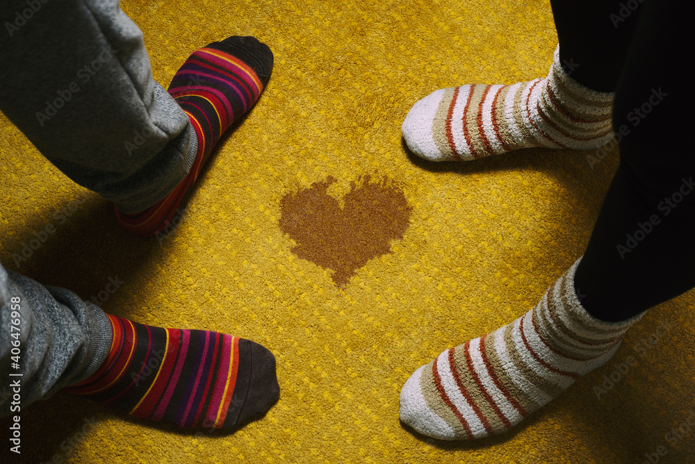 Wall mural love and valentine's day. feet of woman and man with colored socks on yellow carpet and heart shaped stain.