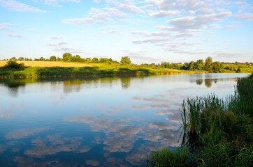 Summer tranquil landscape with river and beautiful reflection of sky clouds on water surface.
