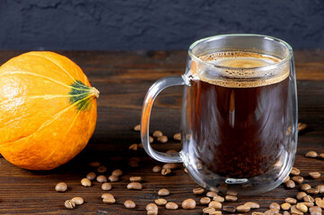 A cup of coffee on wooden table. A glass mug of coffee. Pumpkin on a wooden background. Morning coffee. Marble mortar for grinding grains. Copy space.
